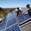 A picture of workers installing solar panels on the roof of a house.