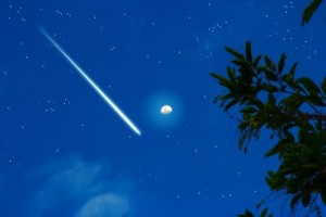 A picture of a beautiful meteorite whizzing through the Earth's atmosphere. with the moon in the background.